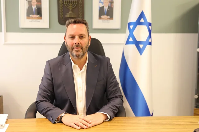 אוהד שגב, ראש עיריית עכו, יושב בלשכתו לצד דגל ישראל